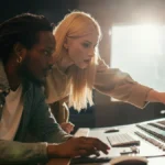 A male producer and a female singer collaborating together in a bright, modern music recording studio.