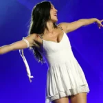 Olivia Rodrigo performs on stage in a white dress with her arms outstretched